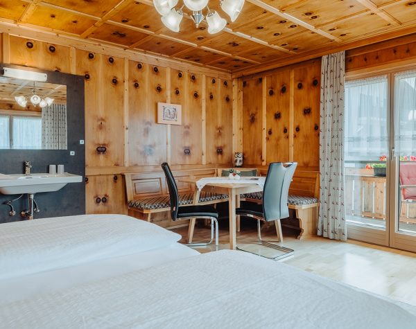 rustikales Schlafzimmer mit Holztafeln an Wand und Decke, Holzboden, Doppelbett, Eckbank neben der Balkontür und Waschbecken