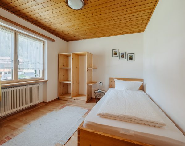helles Schlafzimmer mit Einzelbett, offenes Holzregal, großem Fenster, Holzboden und Holzdecke
