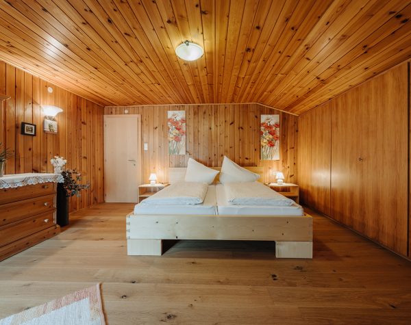 rustikales Schlafzimmer mit Holzvertäfelungen und Einbauschrank, helles Doppelbett aus Holz und rustikale Schubladenkommode