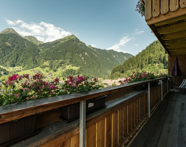 Ausblick auf die Bergwelt von traditionellem Holzbalkon bei Sonnenschein und schönen Blumen am Balkon