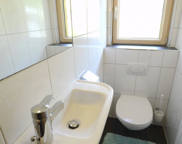 helles kleines WC der kleinen Wohnung mit weißen Wandfließen und grauem Boden