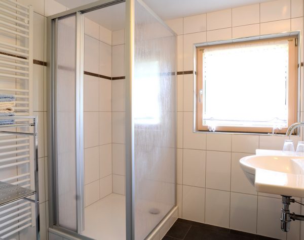 helles Bad mit Dusche, Fenster, weißen Wandfließen, schwarzen Bodenfließen und Waschbecken rechts der Dusche